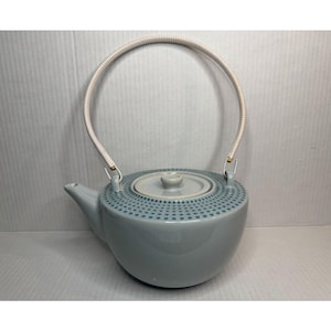 May include: A light blue ceramic teapot with a white and beige handle. The lid and body feature a dotted pattern in a darker blue. The teapot has a spout for pouring and is designed for serving tea.