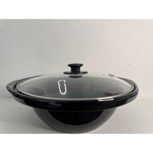 May include: A black slow cooker with a glass lid. The slow cooker has a round shape with a black handle on each side. The glass lid has a black knob on top. The slow cooker is on a white surface.