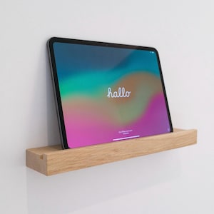 Puede incluir: Una estantería de madera montada en una pared blanca con una tableta apoyada en ella. La pantalla de la tableta muestra un fondo degradado de colores con la palabra "hallo" en texto blanco.