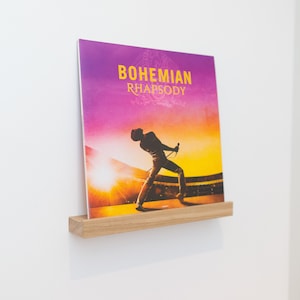 Może przedstawiać: Płyta winylowa w kolorze fioletowym, żółtym i pomarańczowym z sylwetką osoby śpiewającej na scenie. Płyta nosi tytuł "Bohemian Rhapsody".