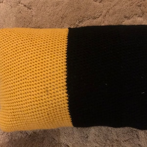 Puede incluir: Una almohada de crochet con un esquema de color amarillo y negro. La almohada está hecha de un hilo suave y texturizado.