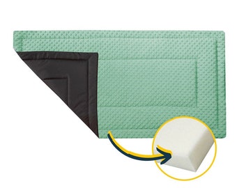 May include: A light green quilted play mat with a black quilted border and a white foam layer underneath. The mat is designed for babies and toddlers.