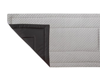 May include: A gray and black quilted baby play mat with a textured surface. The mat is folded in half, revealing the black underside.