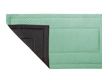 May include: A light green quilted blanket with a black quilted backing. The blanket is folded in half and the backing is visible.