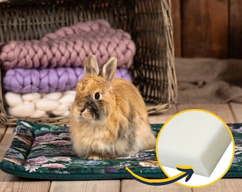 May include: A green and floral patterned pet bed with a white foam insert. A brown and white rabbit is sitting on the bed.