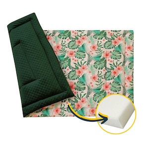 May include: A green and white reversible play mat with a tropical floral print. The mat is filled with foam for cushioning.
