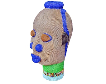 May include: A beaded sculpture of a human head with blue, green, and brown beads. The sculpture is made of small beads that are woven together to create a detailed and intricate design.