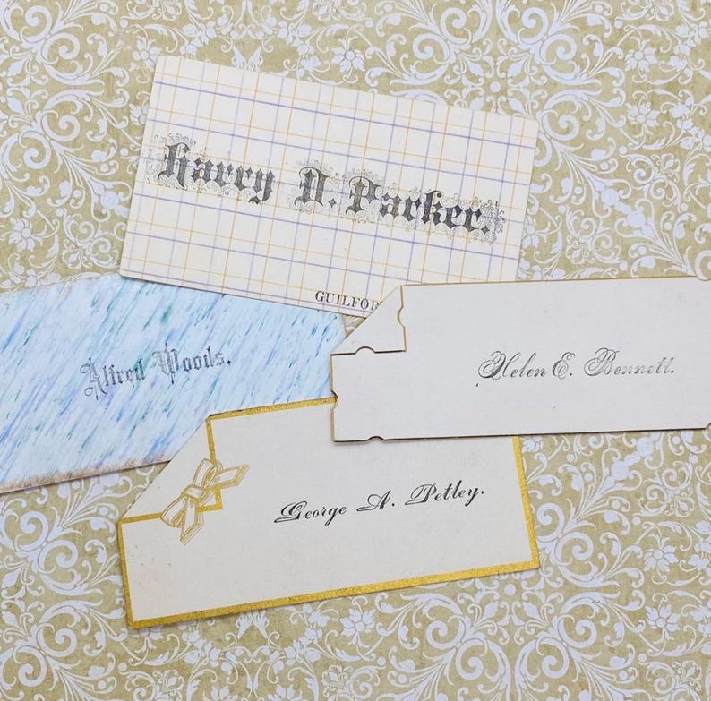 May include: Four vintage place cards with handwritten names in cursive script. The cards are white with gold trim and feature different designs. The names on the cards are Harry N. Packer, Alfred Woods, Helen C. Bennett, and George A. Petley.