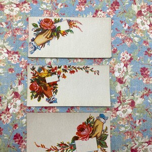 May include: Three vintage blank cards with floral designs. Each card features a hand holding a blank card with a floral design. The cards are on a blue and white floral background.
