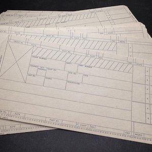 Peut inclure: Une pile de fiches de travail rectangulaires en papier beige clair de The Minster Machine Company. Chaque fiche présente des grilles imprimées en noir, des champs pour le numéro de commande, la date, le numéro de pièce et une échelle de 1 à 84.