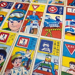 May include: A set of vintage Japanese playing cards featuring illustrations of cars, pedestrians, and traffic signs. The cards are printed on thick paper with bright colors and bold lines. The text on the cards is in Japanese.