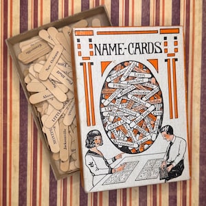 May include: A vintage Name-Cards game box with an open lid revealing wooden sticks printed with city names. The box cover features an oval graphic filled with overlapping city name sticks, flanked by orange geometric designs and illustrations of two people.