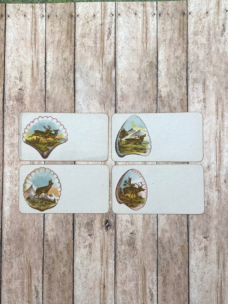 May include: Four vintage place cards with a white background and a seashell design featuring a deer in a forest scene. The seashells are in shades of blue, green, and brown.
