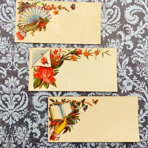 May include: Three vintage blank note cards with floral designs. The top card features a fan, the middle card features a rose, and the bottom card features a hand holding an open book.
