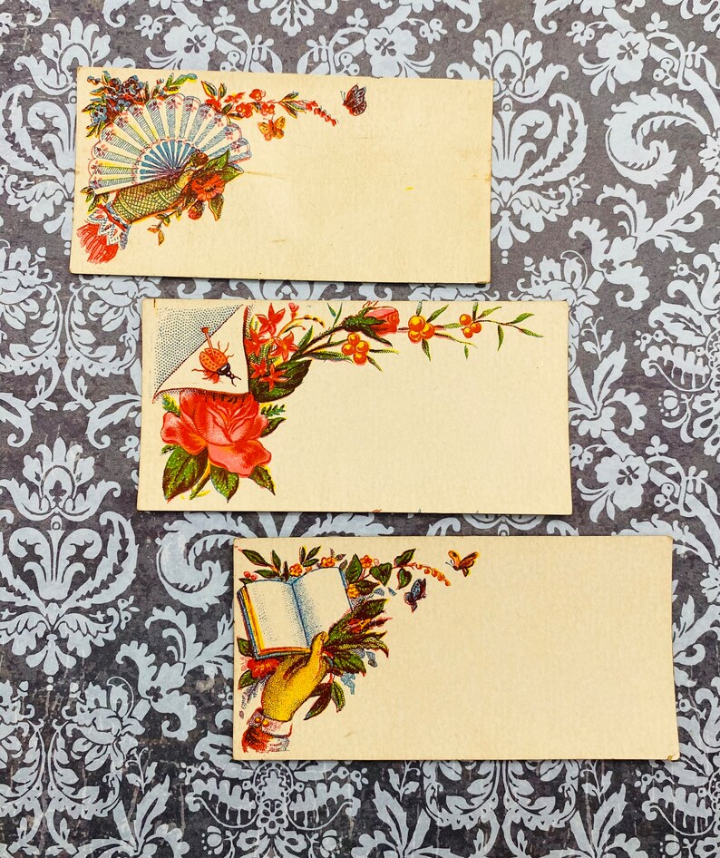 May include: Three vintage blank note cards with floral designs. The top card features a fan, the middle card features a rose, and the bottom card features a hand holding an open book.