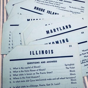 May include: A blue and white card game with the title "Illinois" and questions and answers about the state. The questions include: What is the capital of Illinois? What is the state flower of Illinois? What state is known as The Prairie State? Where is the Field Museum? In what state did Cyrus McCormick make and sell wheat harvesters? In what state is Chicago, Peoria, East St. Louis? The answers are: Springfield, The Violet, Illinois, Illinois, Illinois, Illinois.