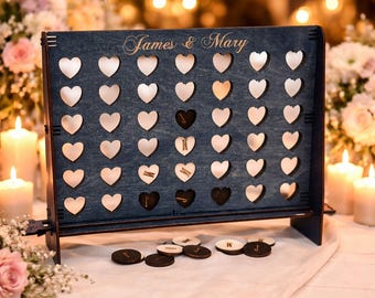 May include: A dark blue wooden game board featuring a grid of heart-shaped cutouts and the engraved text James & Mary. The board includes several circular wooden game pieces with letters scattered at the base, designed for a connect-style game.