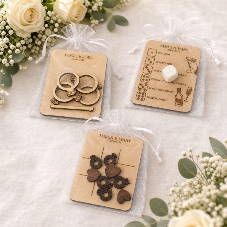 three wooden game pieces with various designs, including rings, hearts, and a tic-tac-toe board, placed on a white background with white flowers.
