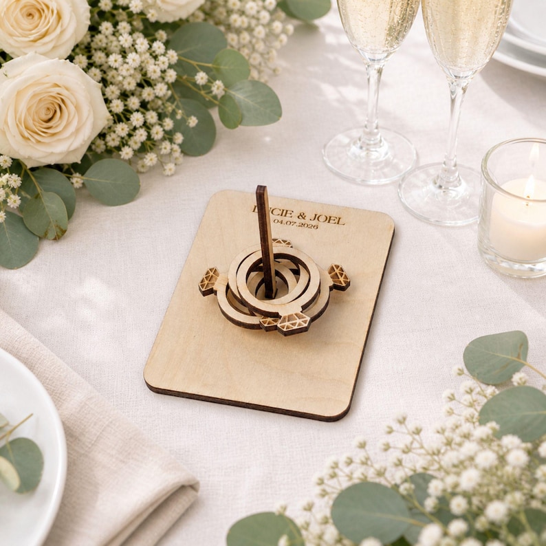 a wooden ring toss game with a wooden ring on top, surrounded by white roses, greenery, and champagne glasses.