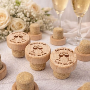 a collection of wooden cork stoppers with engraved text, likely wedding-related, placed on a table with champagne glasses and a floral arrangement in the background.