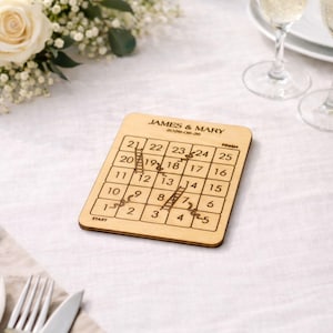A wooden puzzle game with numbers on it, placed on a table with a floral arrangement and wine glasses in the background.