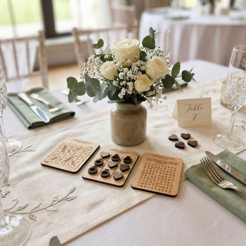 A table setting with a vase of white roses, a card, and a game board with wooden coasters.