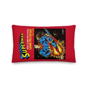 Peut inclure: Coussin rectangulaire rouge avec un graphisme Superman. Le graphisme représente Superman dans une pose dynamique sur fond spatial. Le coussin comporte également le texte "SUPERMAN" et "VIDEO COMPUTER SYSTEM GAME PROGRAM ONE PLAYER".