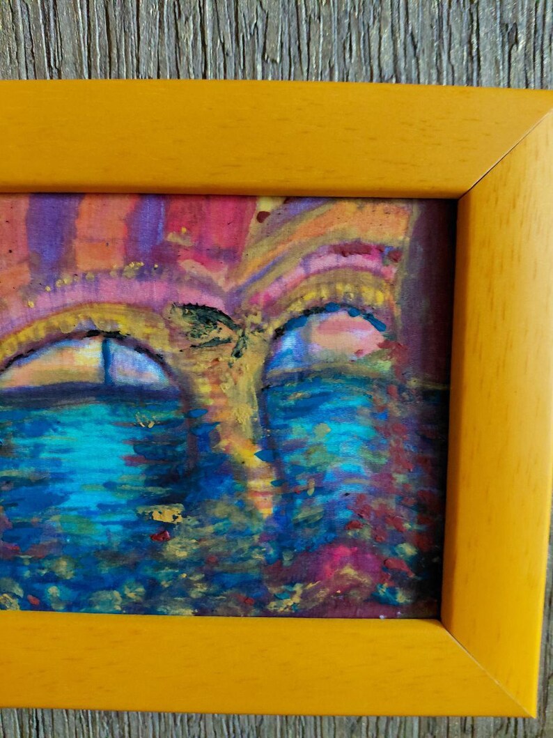 K&ouml;nnte beinhalten: Abstrakte Malerei in einem gelben Rahmen. Das Kunstwerk zeigt eine lebendige Mischung aus Farben, darunter Blau, Rosa und Gelb, die eine traumhafte Landschaft schaffen. Der Stil des Gem&auml;ldes ist impressionistisch, mit sichtbaren Pinselstrichen und einem Fokus auf Farbe und Licht.