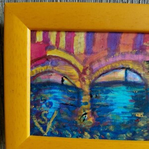 K&ouml;nnte beinhalten: Abstrakte Malerei in einem gelben Rahmen. Das Kunstwerk zeigt eine gesichts&auml;hnliche Komposition mit blauen, gelben, rosa und violetten Farbt&ouml;nen. Das Gem&auml;lde hat ein strukturiertes Aussehen mit sichtbaren Pinselstrichen und einer Signatur in der unteren linken Ecke.