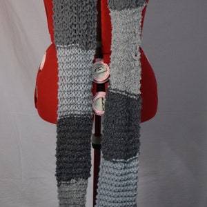 May include: A gray and black knitted scarf with a chunky texture. The scarf is draped over a red dress form.
