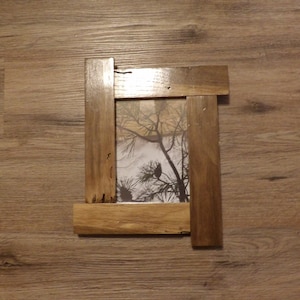 May include: A rustic wooden picture frame with a natural wood finish. The frame has a simple design with a rectangular opening for a photo. The frame is made of reclaimed wood and has a distressed look.