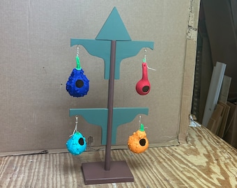 May include: A wooden stand with four gourd birdhouses painted in different colors: blue, red, turquoise, and orange. The stand is painted brown and has a green triangular top.