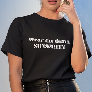May include: A woman wearing a black t-shirt with the text "wear the damn SUNSCREEN" in white letters. She is also wearing a black leather skirt.