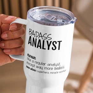 Peut inclure: Mug de voyage blanc avec un design noir qui dit "BADASS ANALYST" et une définition du terme.
