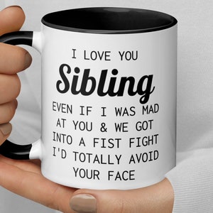 May include: White ceramic coffee mug with a black rim and handle. The mug has black text that reads "I love you Sibling. Even if I was mad at you & we got into a fist fight I'd totally avoid your face."