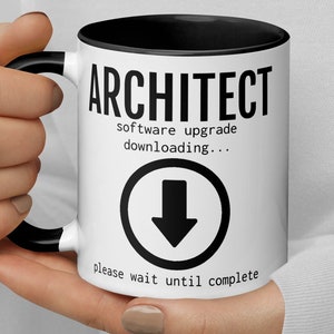 May include: White ceramic mug with a black rim and handle. The mug has black text that reads "ARCHITECT software upgrade downloading..." with a black downward arrow icon and the text "please wait until complete".