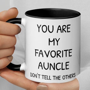 May include: White ceramic mug with a black rim and handle. The mug has black text that reads "You are my favourite auncle. Don't tell the others."