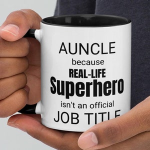 May include: White ceramic mug with a black rim and handle. The mug has black text that reads "AUNCLE because REAL-LIFE SUPERHERO isn't an official JOB TITLE".