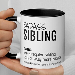 May include: White ceramic mug with a black rim and handle. The mug has black text that reads "BADASS SIBLING" and a definition of the term. The definition reads "noun like a regular sibling, except way more badass see also: superhero, miracle worker"