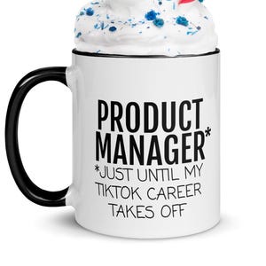 May include: A white coffee mug with a black handle and rim, filled with whipped cream and a red and white striped straw. The mug has the text "PRODUCT MANAGER* *JUST UNTIL MY TIKTOK CAREER TAKES OFF" in black.