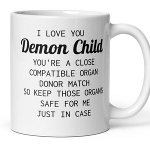 May include: White ceramic coffee mug with black text that reads "I love you Demon Child You're a close compatible organ donor match so keep those organs safe for me just in case."