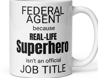 May include: White ceramic mug with black text that reads "Federal Agent because Real-Life Superhero isn't an official Job Title".