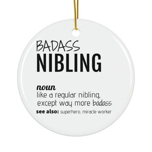 May include: White ceramic bauble with black text that reads "BADASS NIBLING" and a definition of the word. The definition reads "noun like a regular nibling, except way more badass see also: superhero, miracle worker"