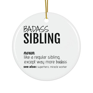 May include: White ceramic ornament with black text that reads "BADASS SIBLING noun like a regular sibling, except way more badass see also: superhero, miracle worker"