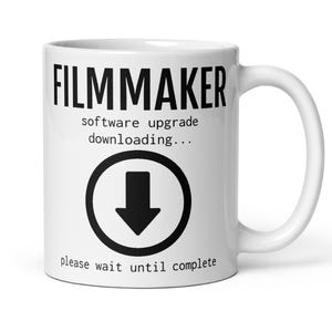 May include: White ceramic mug with the word "FILMMAKER" in bold black letters. Below, the text reads "software upgrade downloading..." and "please wait until complete." A black circle with a downward arrow is in the center.