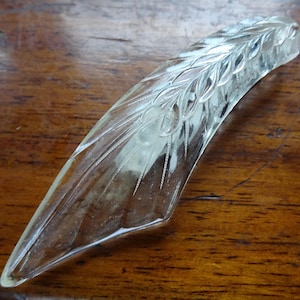 May include: A clear glass decorative handle with a floral design. The handle is curved and has a pointed end.