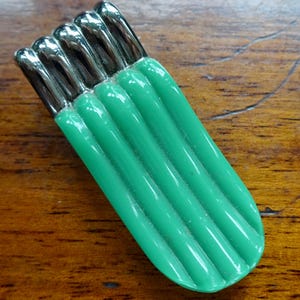Puede incluir: Un broche vintage verde y plateado con un diseño acanalado. El broche tiene forma de rectángulo largo y delgado con extremos redondeados.