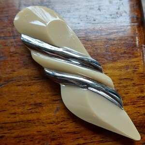 Puede incluir: Un broche de plástico beige con un diseño de espiral plateado.