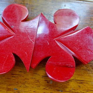 May include: A close-up of a bright red, abstract wooden object. The object is composed of several geometric shapes, including circles, triangles, and a diamond. The surface shows visible scratches, suggesting it is vintage or well-used.