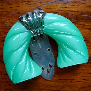 May include: A vintage green plastic hair clip with a silver metal clasp. The clip is shaped like a half-circle and has a twisted design.